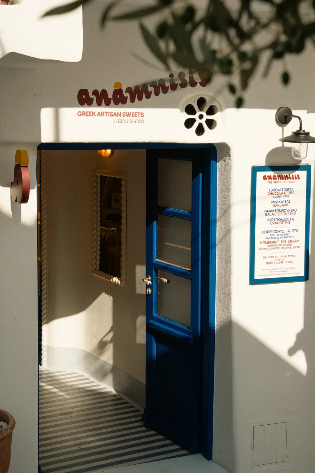 The Anamnisis doorway — blue door, painted sign and morning shade